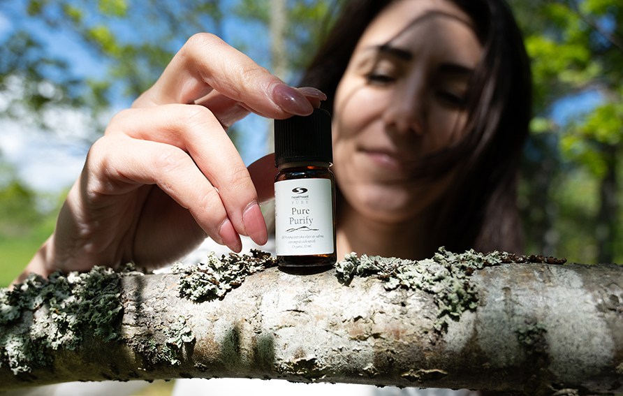Nainen pitelee PURE Purify -pulloa puun oksalla
